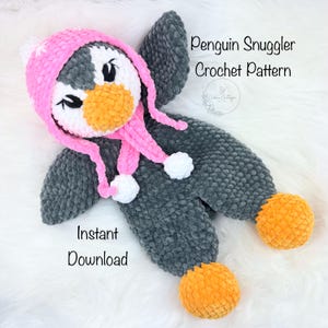 May include: A handmade crochet penguin snuggler in gray, white, pink, and orange. The penguin has a pink hat with ear flaps and white pom-poms. The text "Penguin Snuggler Crochet Pattern" and "Instant Download" are visible.