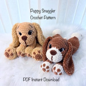 May include: Two crochet puppy dog toys in shades of brown and tan. One is light brown with a dark brown nose, and the other is brown and white. The text "Puppy Snuggler Crochet Pattern" and "PDF Instant Download" are visible.