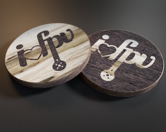 May include: Two round wooden coasters with a brown wood grain pattern. The coasters feature the text "i love fpv" in a dark brown color. One coaster has a light wood grain and the other has a dark wood grain.