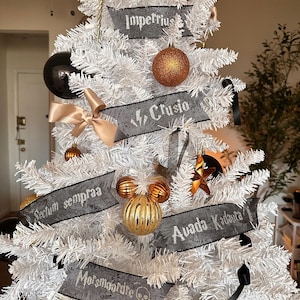 May include: A white artificial Christmas tree decorated with black and gold ornaments. Black ribbons with white text spell out spells like "Imperius" and "Crucio". Gold and black baubles and a gold bow add to the festive look.