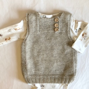 Op de afbeelding: Een lichtbruin gebreid vest met knoopsluiting. Het vest heeft een eenvoudig ontwerp en is gemaakt van een zacht, comfortabel materiaal.