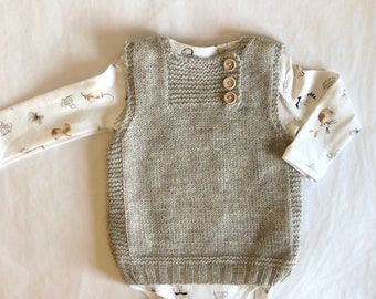 May include: A light brown knitted waistcoat with a button fastening. The waistcoat has a simple design and is made of a soft, cosy material.