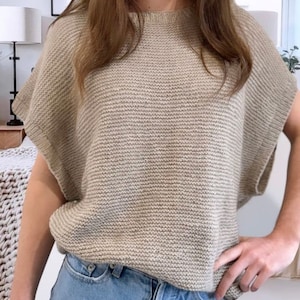 May include: A beige knitted sweater with short sleeves and a round neckline.