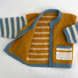 Pode incluir: Um cardigan de malha listrado amarelo e azul com um bolso na frente. O cardigan está aberto e o interior é visível, mostrando um padrão listrado amarelo e branco.
