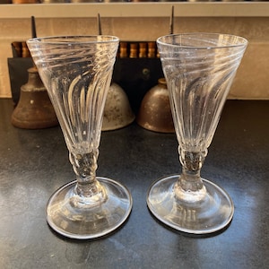 Può includere: Due bicchieri da vino in vetro trasparente con stelo e design a spirale. I bicchieri sono su una superficie scura.