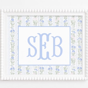 May include: A framed print featuring a light blue monogram with the letters SEB centered on a white background. The border displays a repeating vertical pattern of blue and pink floral vines on a white background with thin blue stripes.