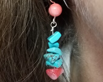 May include: A dangling earring featuring a coral-colored bead at the top, followed by a series of turquoise-colored stone chips and a red shell-shaped bead. The earring is suspended from a silver-colored hook.