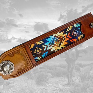 May include: A brown leather guitar strap with a colorful geometric pattern. The strap has a silver concho on one end and a brown leather loop on the other end.