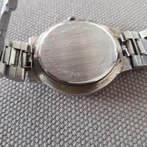 Puede incluir: La parte posterior de un reloj de pulsera plateado con una correa de acero inoxidable. La esfera del reloj est&aacute; en blanco y la parte posterior del reloj tiene el texto "WATER RESISTANT", "STAINLESS BACK", "22MM", "QUARTZ" y "JAPAN MVT".