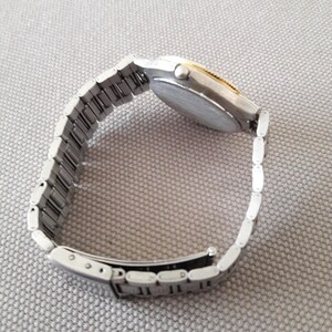 Puede incluir: Un reloj de pulsera plateado y dorado con una banda de metal plateado. El reloj tiene una esfera redonda y un bisel plateado.