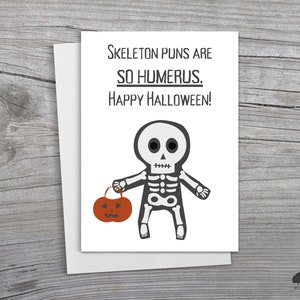 May include: A white card with black text that reads "Skeleton puns are so humerus. Happy Halloween!" and a black and white cartoon skeleton holding a small orange pumpkin.