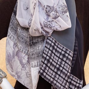 May include: A collection of silk scarves in various patterns and colors. The scarves include floral, geometric, and plaid designs in shades of gray, white, and black. The scarves are draped over a mannequin, showcasing the different textures and styles.