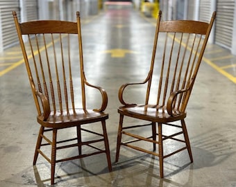 May include: Two antique wooden rocking chairs with tall backs and curved armrests. The chairs have a light brown finish and are set against a neutral background. The chairs have a classic, traditional design.