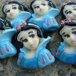 May include: A set of ten small, colorful, ceramic figurines of Snow White. Each figurine is about 1 inch tall and features a different pose of Snow White. The figurines are painted in shades of blue, pink, white, and black.