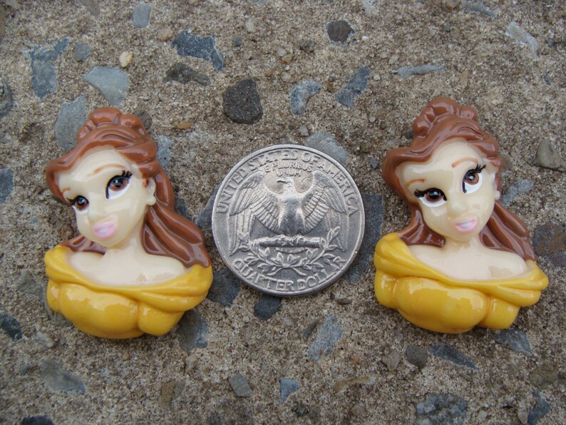 May include: Two yellow and brown Belle character figurines from the Disney movie Beauty and the Beast. The figurines are about the size of a US quarter.