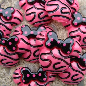 Puede incluir: Botones de resina rayados en rosa y negro con un lazo negro y lunares rosas.