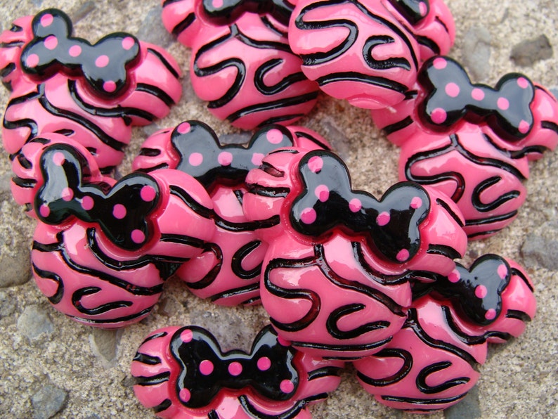 Puede incluir: Botones de resina rayados en rosa y negro con un lazo negro y lunares rosas.