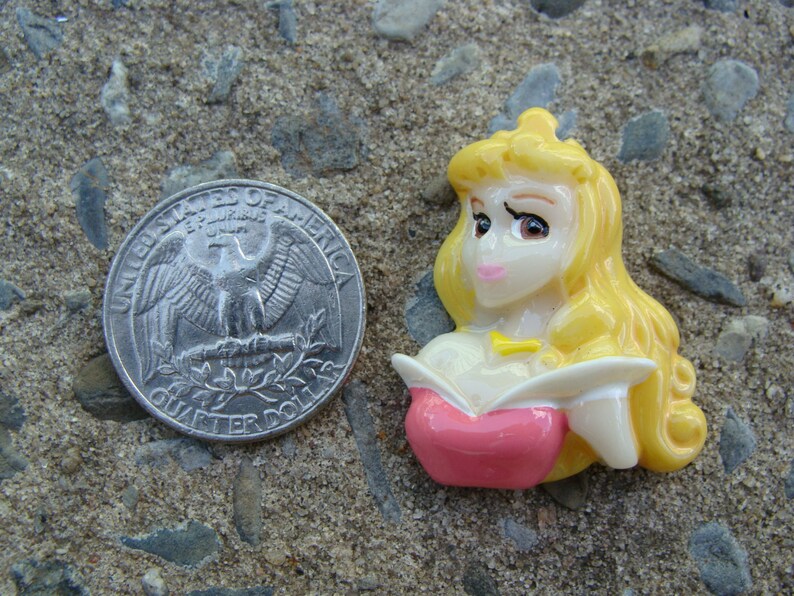 May include: A yellow and pink plastic figurine of a princess with long blonde hair. She is wearing a pink dress and a gold necklace.