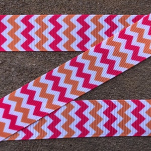 May include: A white ribbon with a chevron pattern in orange and pink. The ribbon is folded in half, with the chevron pattern facing outwards.