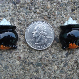 Puede incluir: Dos adornos de Halloween de caldero negro con espuma blanca en la parte superior. Los calderos son aproximadamente del tama&ntilde;o de una moneda de 25 centavos de d&oacute;lar estadounidense.