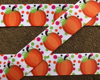 May include: White ribbon with a repeating pattern of orange pumpkins with green stems and brown eyes. The background is white with pink, green, and black polka dots.