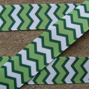 May include: Green and white chevron patterned ribbon. The ribbon features a repeating zigzag design in shades of green and white. The ribbon is made of a textured material, likely grosgrain or similar, and is suitable for crafts and decorations.