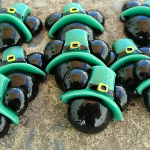 May include: Nine black and green Mickey Mouse-shaped charms with a shamrock design. The charms are made of glass and have a shiny finish.