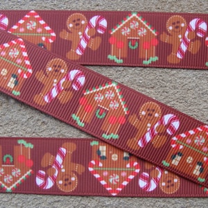 May include: Brown ribbon with a repeating pattern of gingerbread houses and gingerbread people holding candy canes. The houses have green trim and red candy accents. The gingerbread people are brown with white icing and red candy canes.