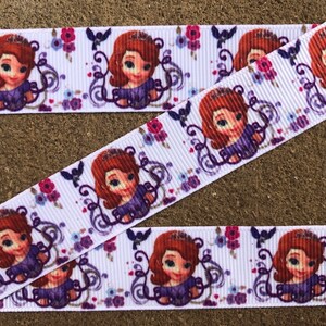 May include: A white grosgrain ribbon featuring a repeating pattern of a cartoon girl with brown hair and a purple dress, accented by small purple birds and clusters of pink and blue flowers. The ribbon has a distinct ribbed texture throughout.