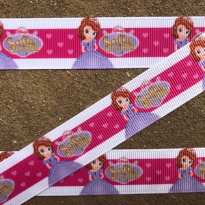 May include: White and pink ribbon with a repeating pattern of a cartoon princess, hearts, and the text "Disney Sofia the First".