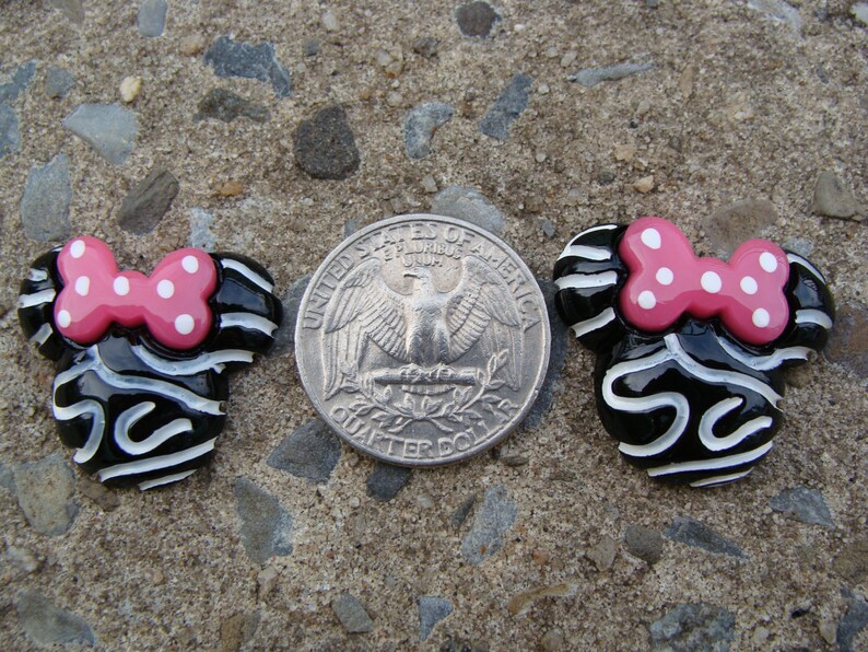 May include: Two black and white ceramic Minnie Mouse head ornaments with pink polka dot bows. The ornaments are about the size of a US quarter.