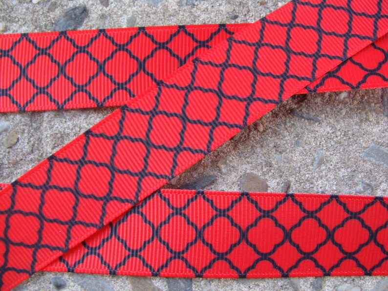 May include: Red ribbon featuring a black quatrefoil pattern. The ribbon has a ribbed texture and is shown in a close-up view. The design is a repeating geometric pattern.