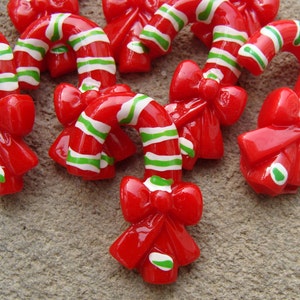 May include: Red and white candy cane ornaments with green stripes and red bows. The ornaments are made of plastic and have a glossy finish.