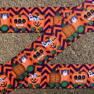 May include: Orange and purple ribbon with a repeating pattern of pumpkins and ghosts riding on a train. The pumpkins have jack-o-lantern faces and the ghosts are white with black eyes.