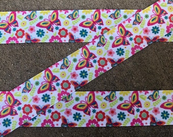 May include: White ribbon with a repeating pattern of colorful butterflies and flowers. The butterflies have yellow, pink, and blue wings. The flowers are pink, red, and blue. The ribbon is suitable for crafts, gift wrapping, or other decorative uses.