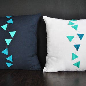 May include: Two decorative throw pillows with a line of teal blue triangles sewn on each. One pillow is navy blue and the other is white.