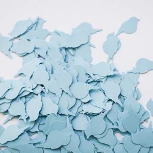 May include: A collection of pale blue bird-shaped paper cutouts. The cutouts are arranged on a white background, creating a decorative effect. The shapes are consistent, suggesting they are for crafting or embellishment purposes.