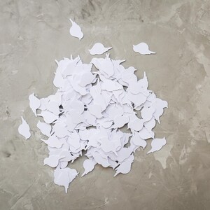 May include: A pile of white, bird-shaped paper cutouts on a grey, textured surface. The cutouts are clustered together, with a few pieces scattered around. The image is taken from a top-down perspective.