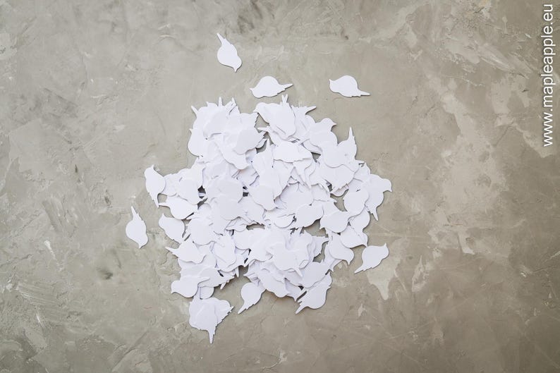 May include: A pile of white, bird-shaped paper cutouts on a grey, textured surface. The cutouts are clustered together, with a few pieces scattered around. The image is taken from a top-down perspective.