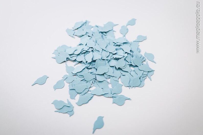May include: A pile of light blue bird-shaped paper cutouts on a white background. The cutouts are in various sizes and shapes, with some scattered around the main pile. The image has a simple, clean design, with a focus on the bird shapes.