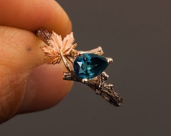 May include: A pear-shaped blue gemstone ring set in a gold band with a twig and leaf design.