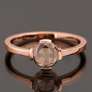 May include: A rose gold ring with a round, faceted, brown gemstone.
