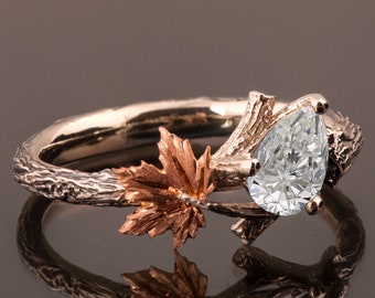 May include: A pear-shaped diamond engagement ring set in a rose gold band with a twig and leaf design. The ring features a delicate maple leaf on the side.