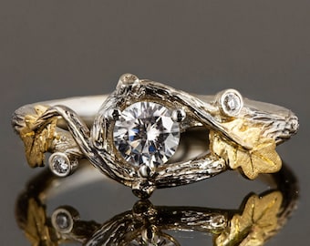 Puede incluir: Un anillo de plata y oro con un gran diamante redondo y claro engastado en un diseño de rama. El anillo presenta dos diamantes más pequeños y detalles de hojas de oro.