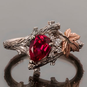Könnte beinhalten: Ein silberner Ring mit einem birnenförmigen Rubin, der in einem astförmigen Design gefasst ist. Der Ring hat auch ein kleines Blattdesign mit einem goldenen Akzent.