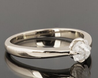 May include: A simple silver band ring with a rough, clear diamond set in the center.