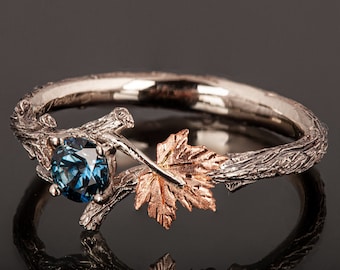 May include: A silver ring with a blue gemstone set in a branch design. The ring features a leaf detail in rose gold.