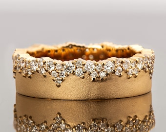 Puede incluir: Un anillo de banda de oro con una fila de pequeños diamantes engastados en un patrón ondulado alrededor del borde superior.