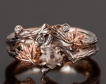 May include: A delicate ring featuring a rough-cut diamond set in a branch and leaf design. The ring is made of two-toned metal, with a rose gold band and a silver branch and leaf design.