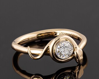 Puede incluir: Un anillo de oro con un diamante engastado en un engaste de bisel. El anillo presenta un diseño de serpiente con la cabeza de la serpiente envolviendo el diamante.